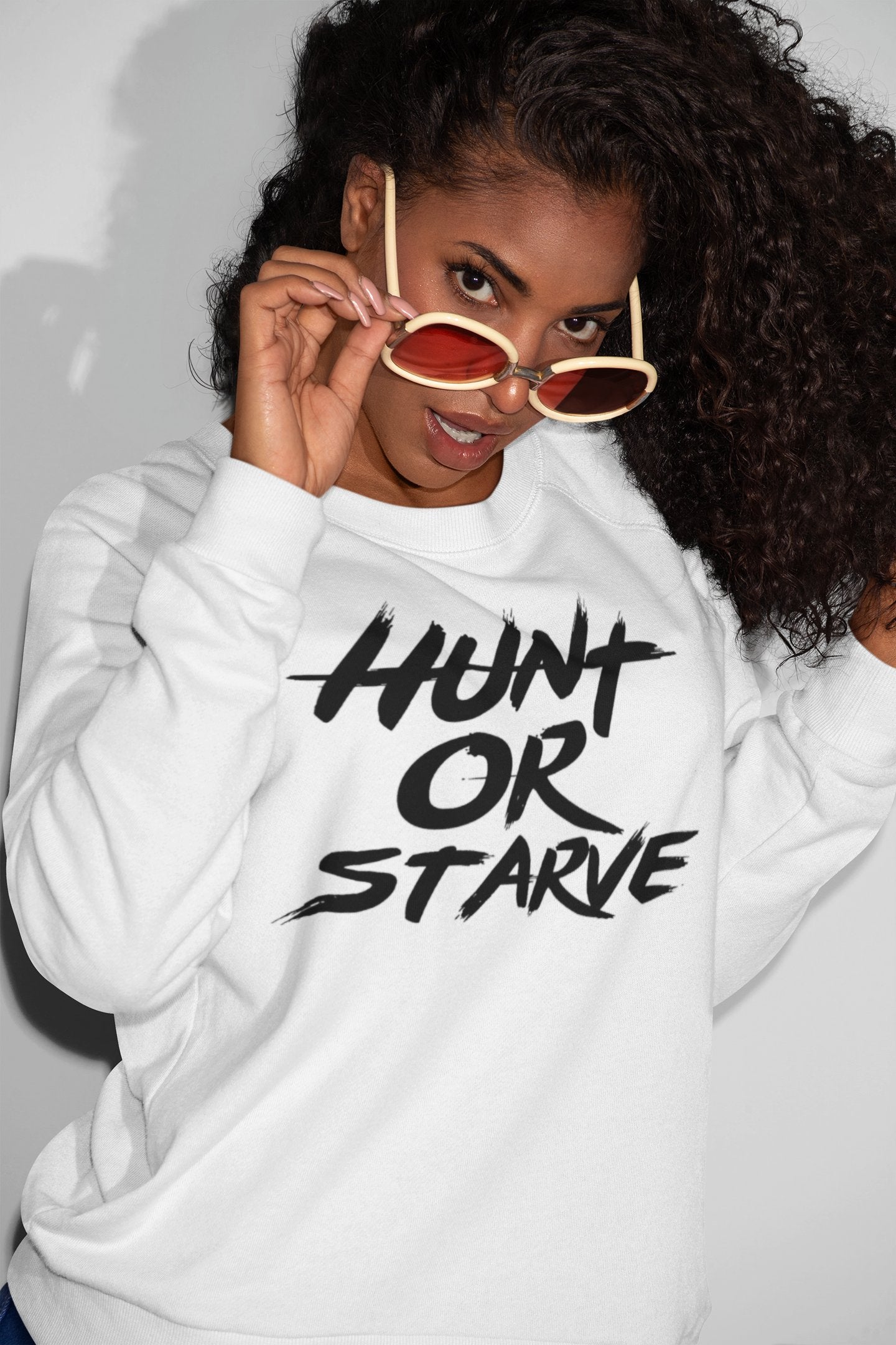 A woman wears a 'Hunt or Starve' slogan sweatshirt, exuding confidence and determination.