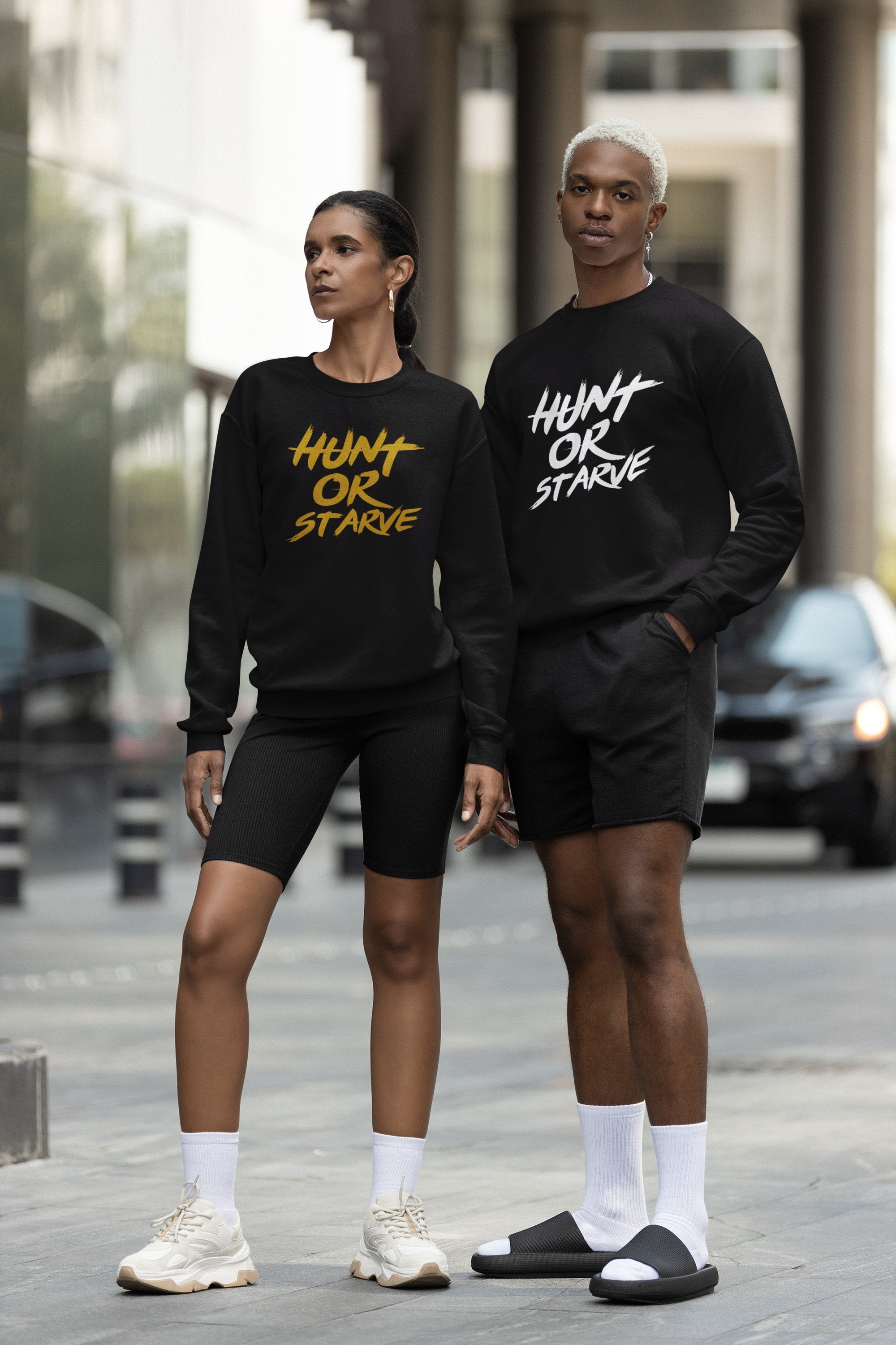 Image: A male and a female model stand side by side, both wearing black crewneck sweatshirts with 'Hunt or Starve' in white lettering. Their confident poses emphasize the empowering message of the apparel