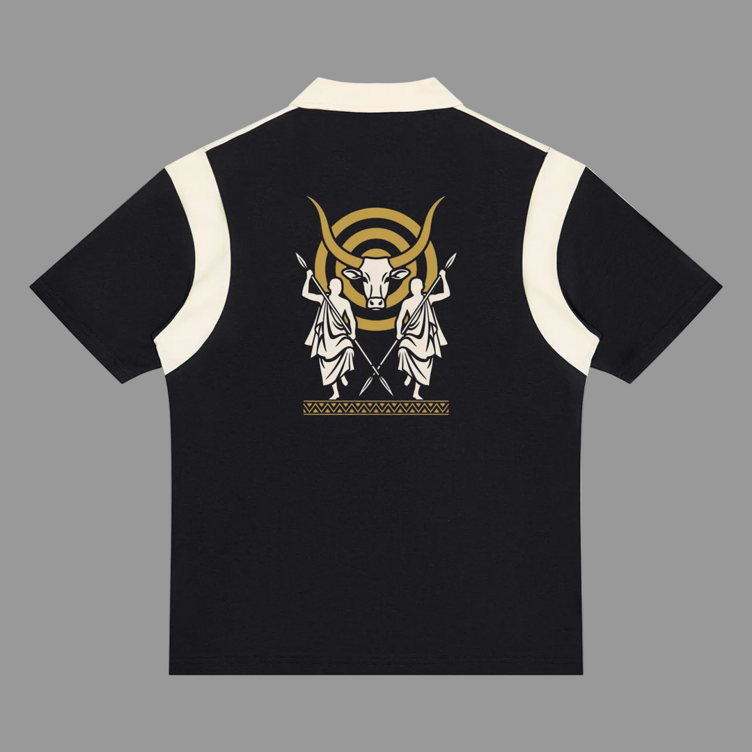 A black short-sleeve polo shirt with cream-colored shoulder panels and collar, featuring a large graphic print on the back with two white classical figures, a gold bull head, and a gold crescent moon.