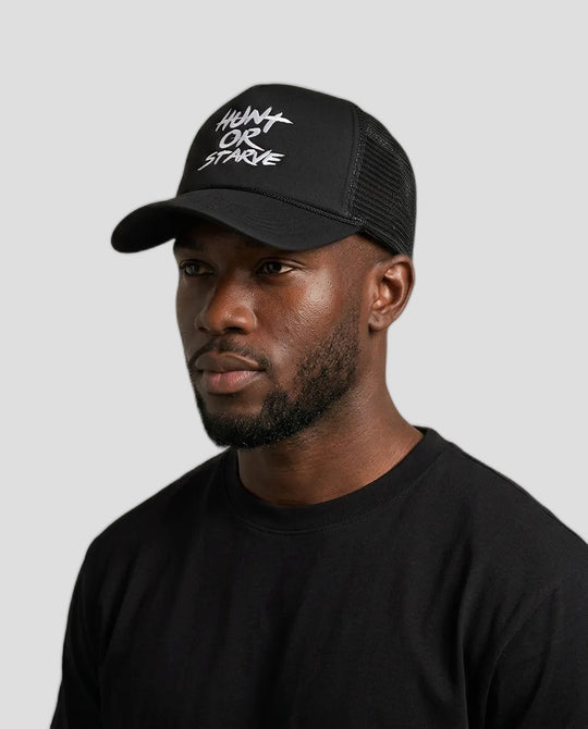 Chris wearing the Relentless HUNT OR STARVE Foam Trucker Hat in black with white brush lettering, grey studio background