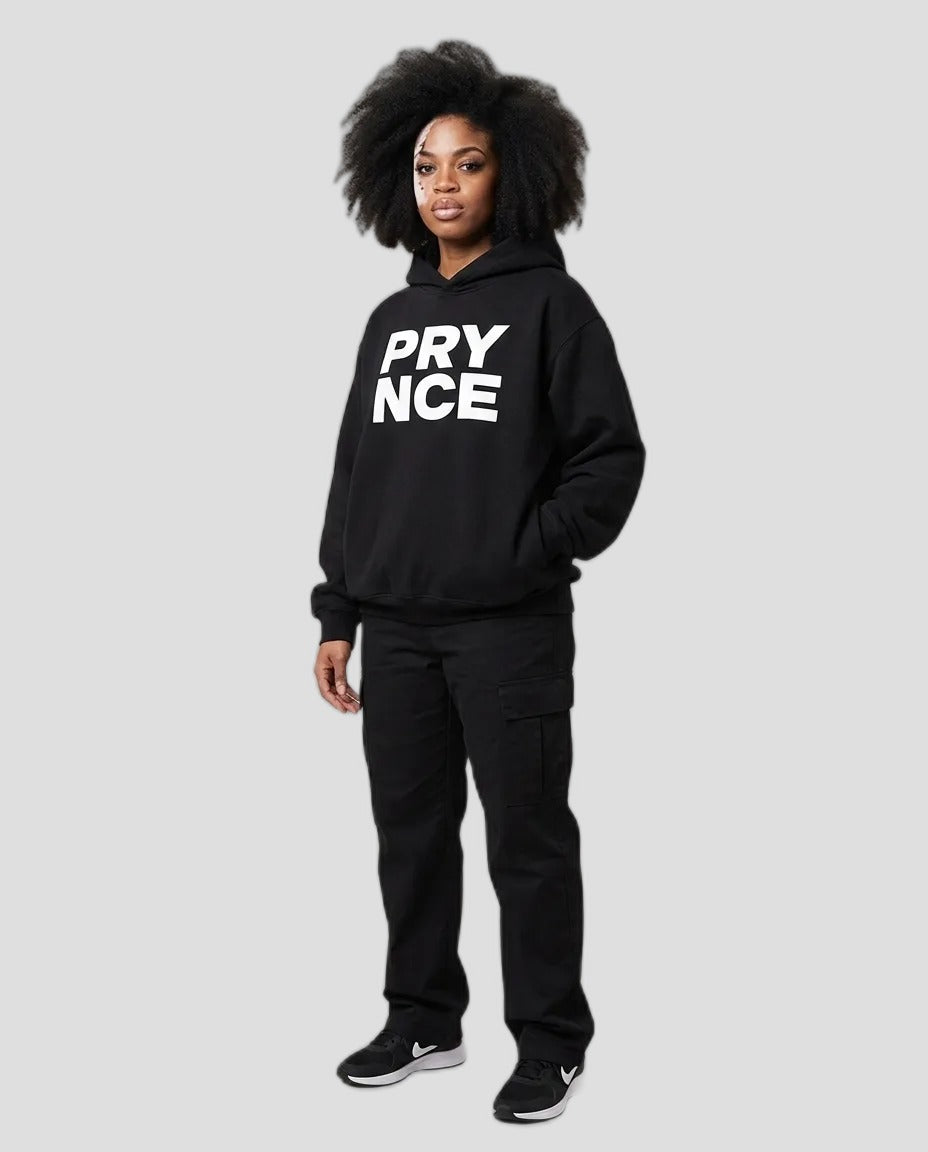 Woman wearing the PRYNCE Monument Boxy Hoodie in black with white stacked PRY NCE print, with black pants