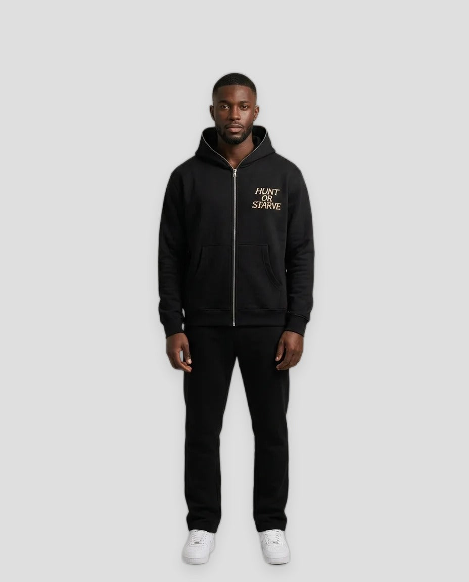 A man modeling a black zip-up hoodie with a gold 'MONT SAINT-MARC' logo on the chest, paired with black pants and white sneakers, against a neutral beige studio background.