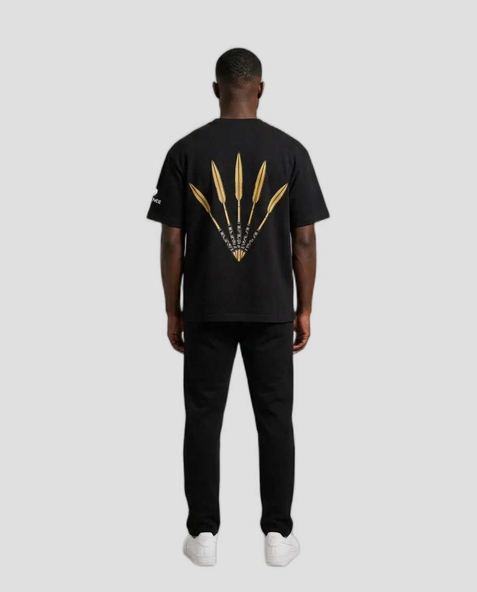 A man viewed from the back wearing a black t-shirt with a large gold graphic of three feathers on the back, paired with black pants and white sneakers, against a neutral beige background.