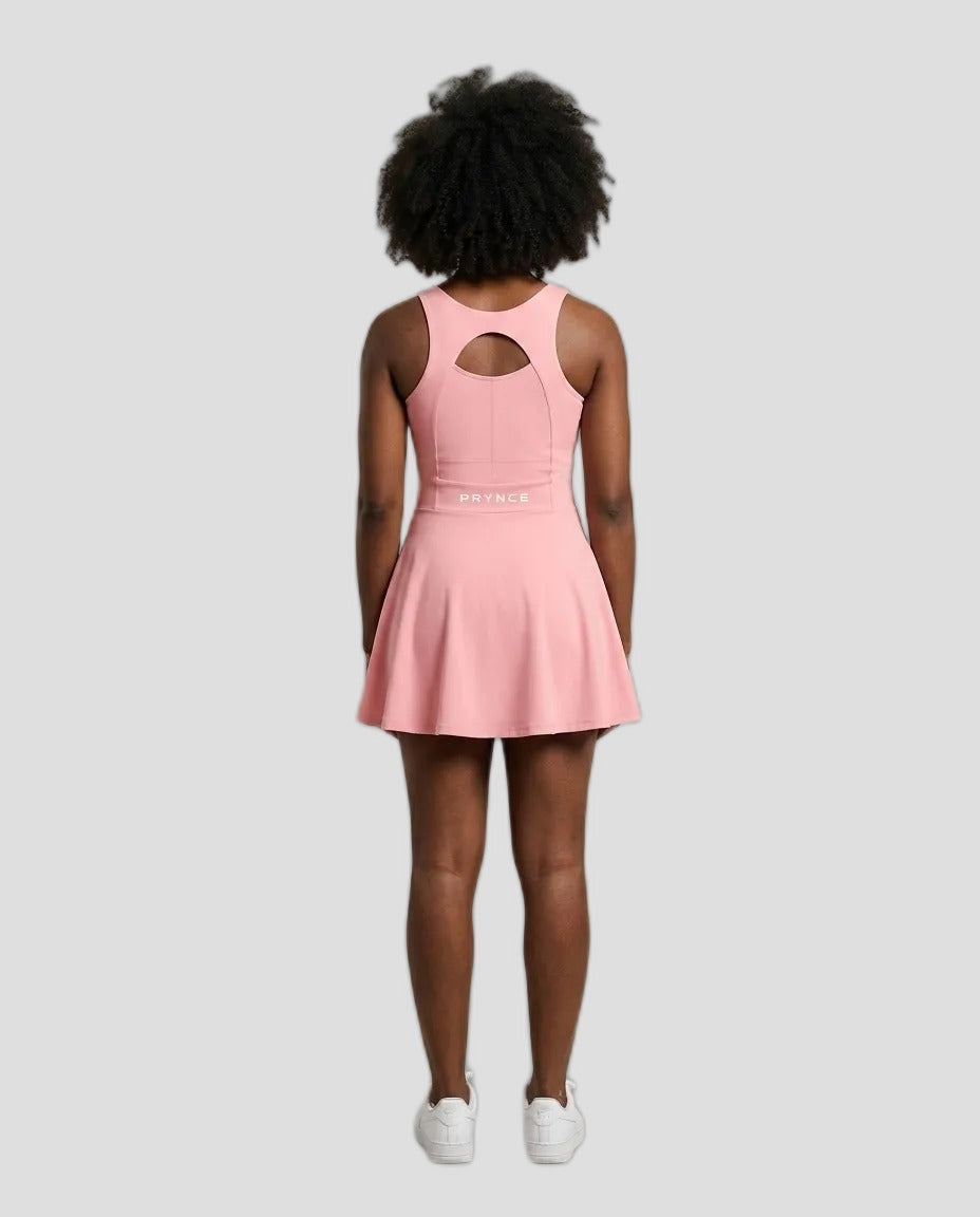 A model viewed from behind wearing a pink sleeveless athletic dress with a keyhole cutout at the back and a flared skirt, paired with white sneakers, against a solid light grey background.