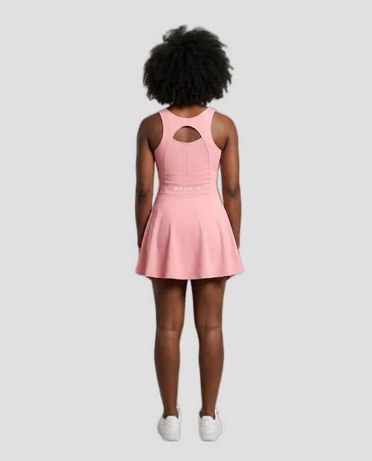 A model viewed from behind wearing a pink sleeveless athletic dress with a keyhole cutout at the back and a flared skirt, paired with white sneakers, against a solid light grey background.