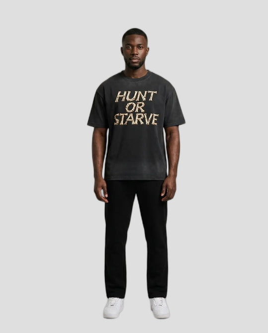 Man wearing the Washed Hunt or Starve Bone Tee in washed black with tan bone-letter HUNT OR STARVE print
