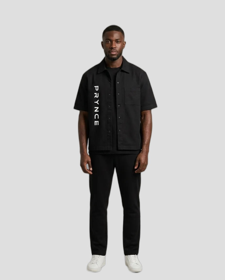 Man wearing the PRYNCE Utility Overshirt in black with vertical PRYNCE lettering, with black pants