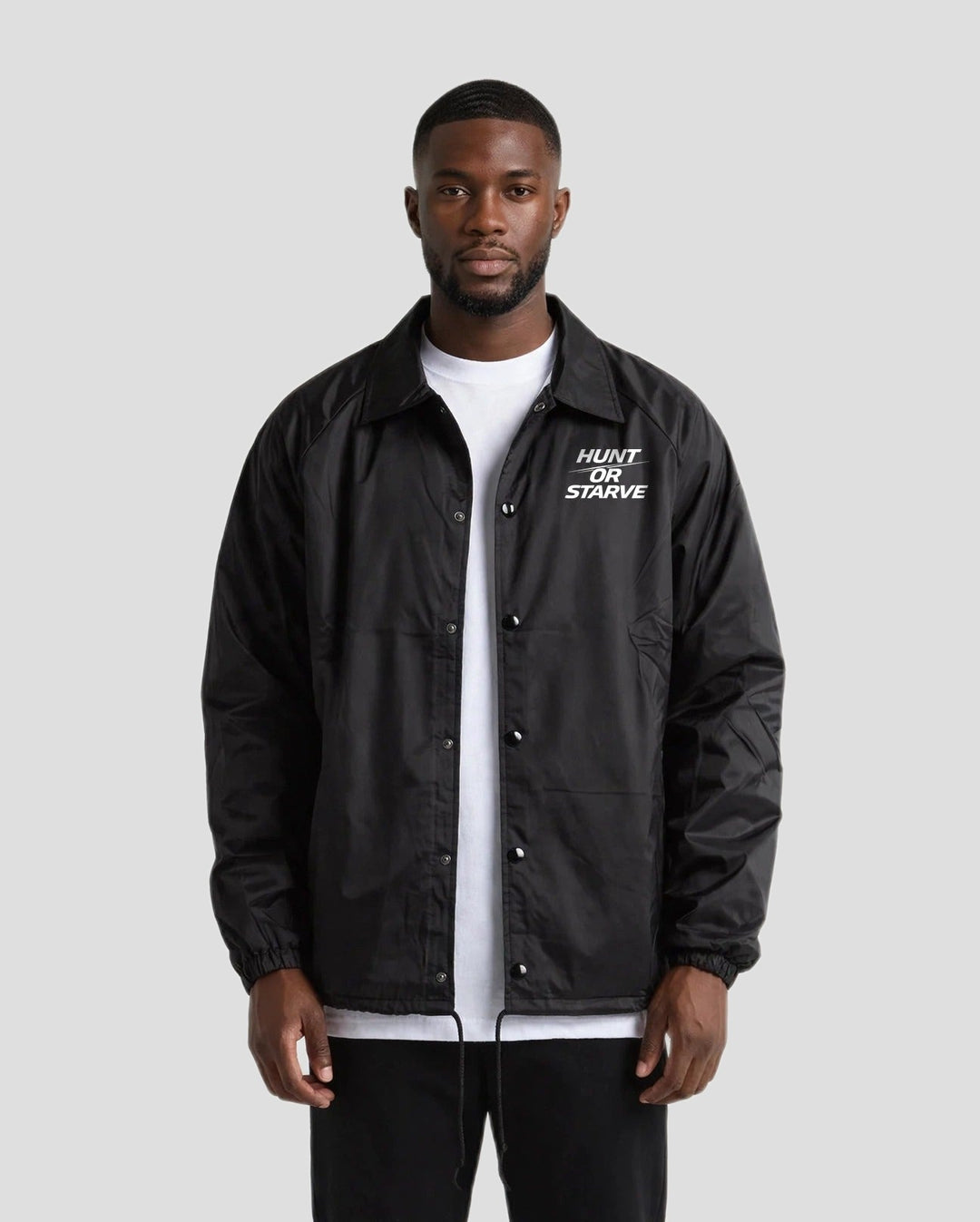 Man wearing the Hunt or Starve Coaches Jacket in black over a white t-shirt, front view