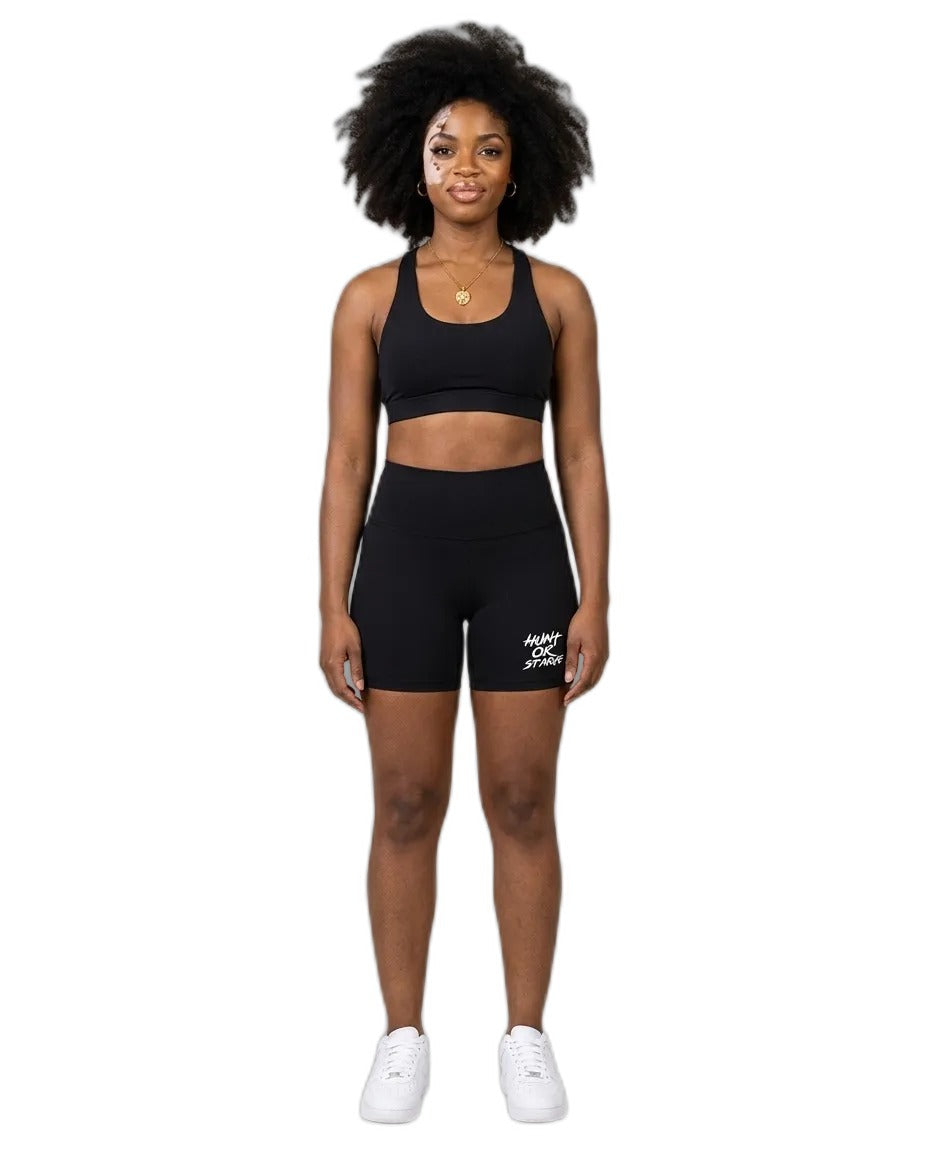 Woman wearing Hunt or Starve Pounce Yoga Shorts in black with a black sports bra, studio photo