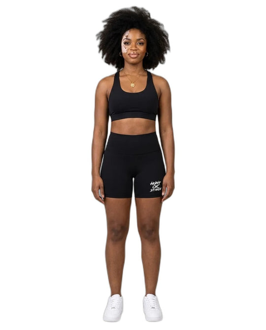 Woman wearing Hunt or Starve Pounce Yoga Shorts in black with a black sports bra, studio photo