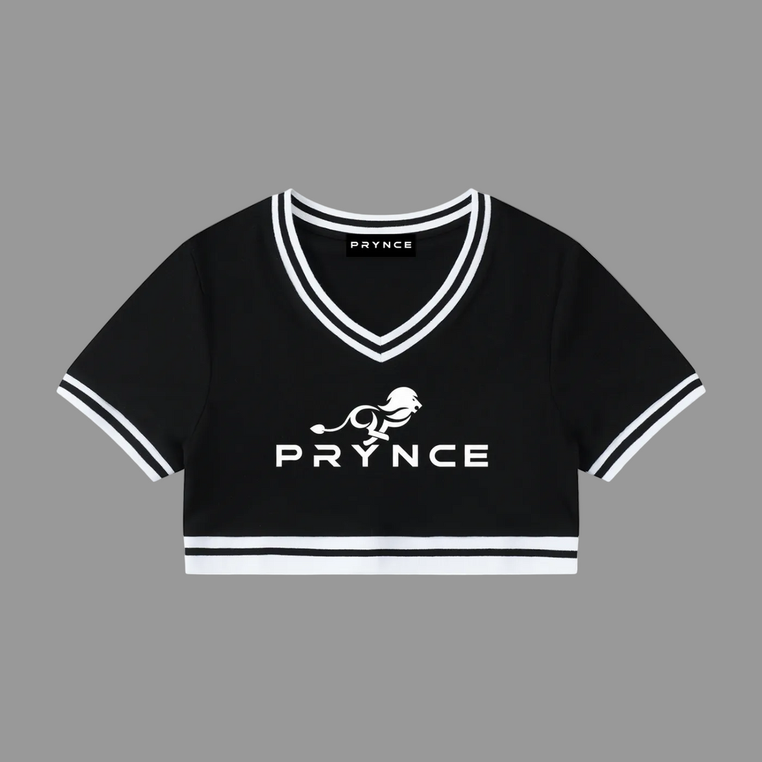 A black short-sleeve cropped V-neck top with white trim and a white printed PRYNCE logo and lion graphic on the front, shown on a plain white background.
