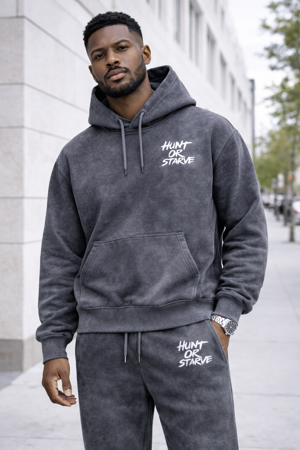 Man wearing a gray hoodie and pants with 'Hunt or Starve' text, standing outdoors.
