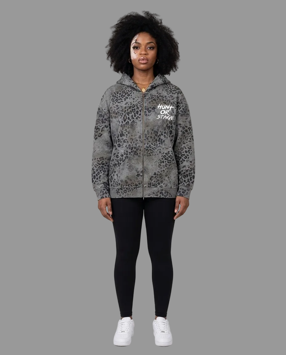 A model stands against a neutral beige studio background wearing a gray and black leopard-print zip-up hoodie with &
