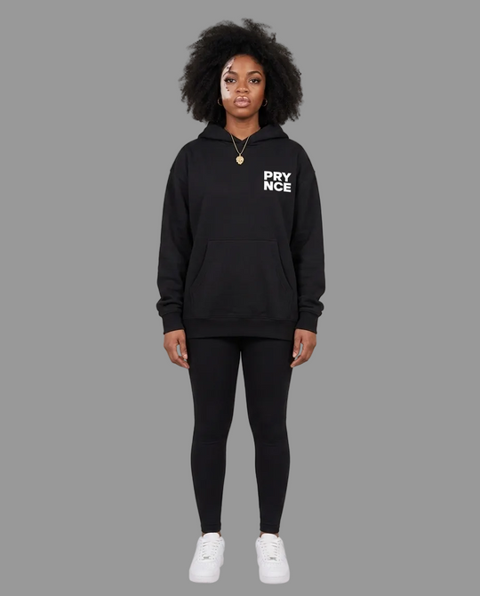 A model stands against a neutral beige studio background wearing a black pullover hoodie with &