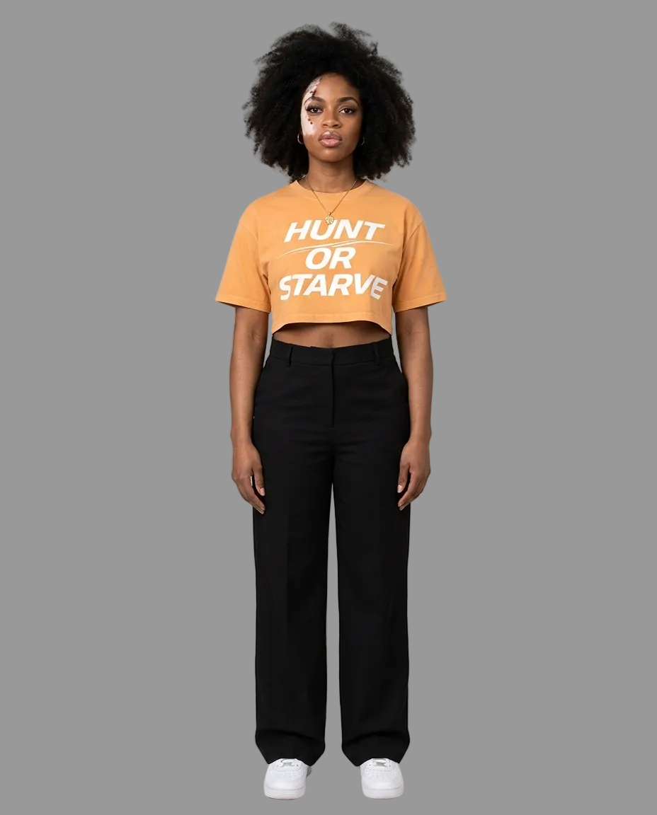 A model stands against a plain beige studio background wearing a cropped orange t-shirt with the text &