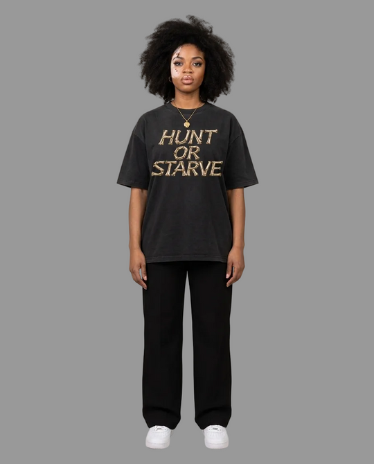 A model stands against a neutral beige studio background wearing a black graphic t-shirt with the words &