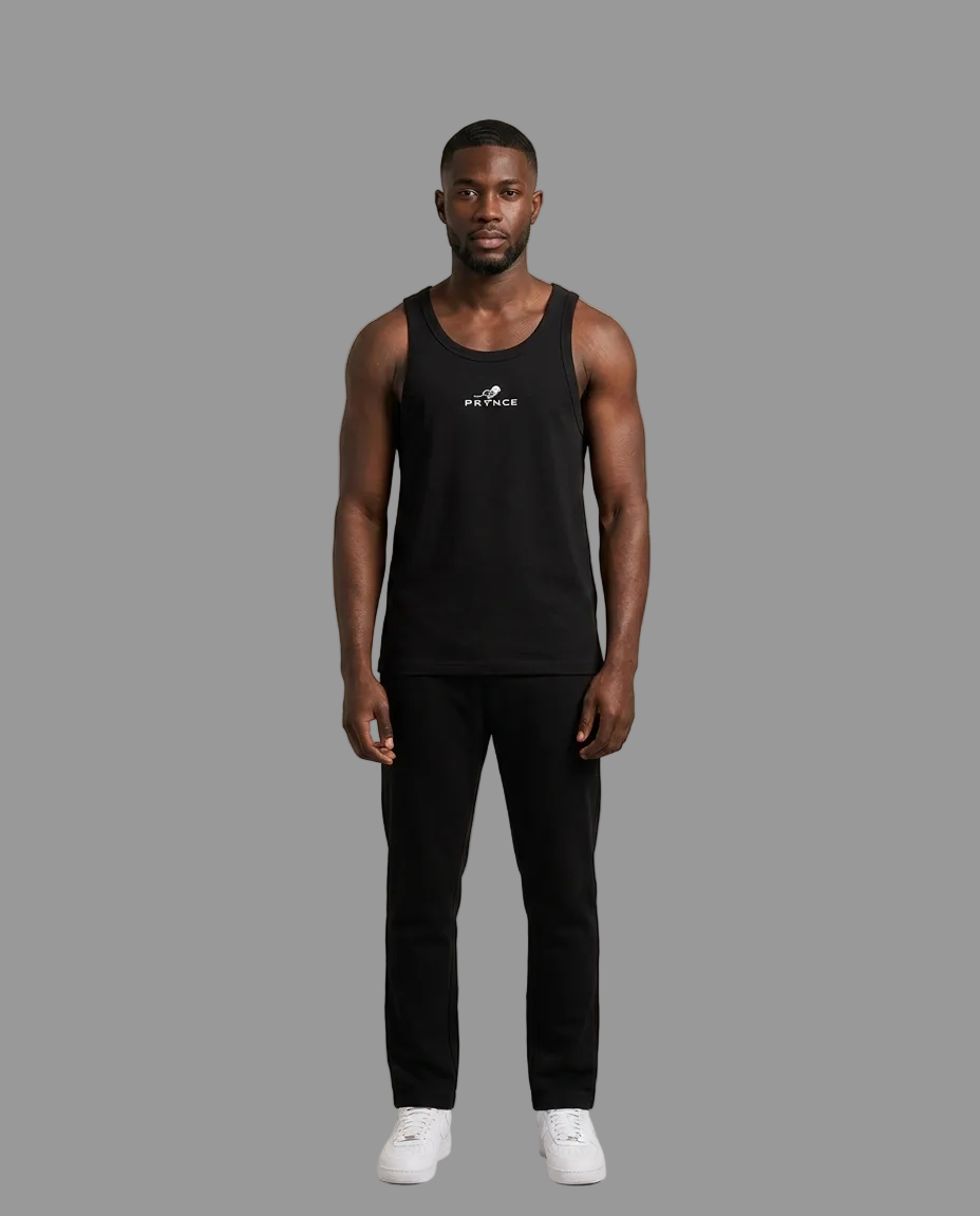 A man modeling a black sleeveless tank top with a small white logo on the chest, paired with black pants and white sneakers, standing against a plain grey studio background.