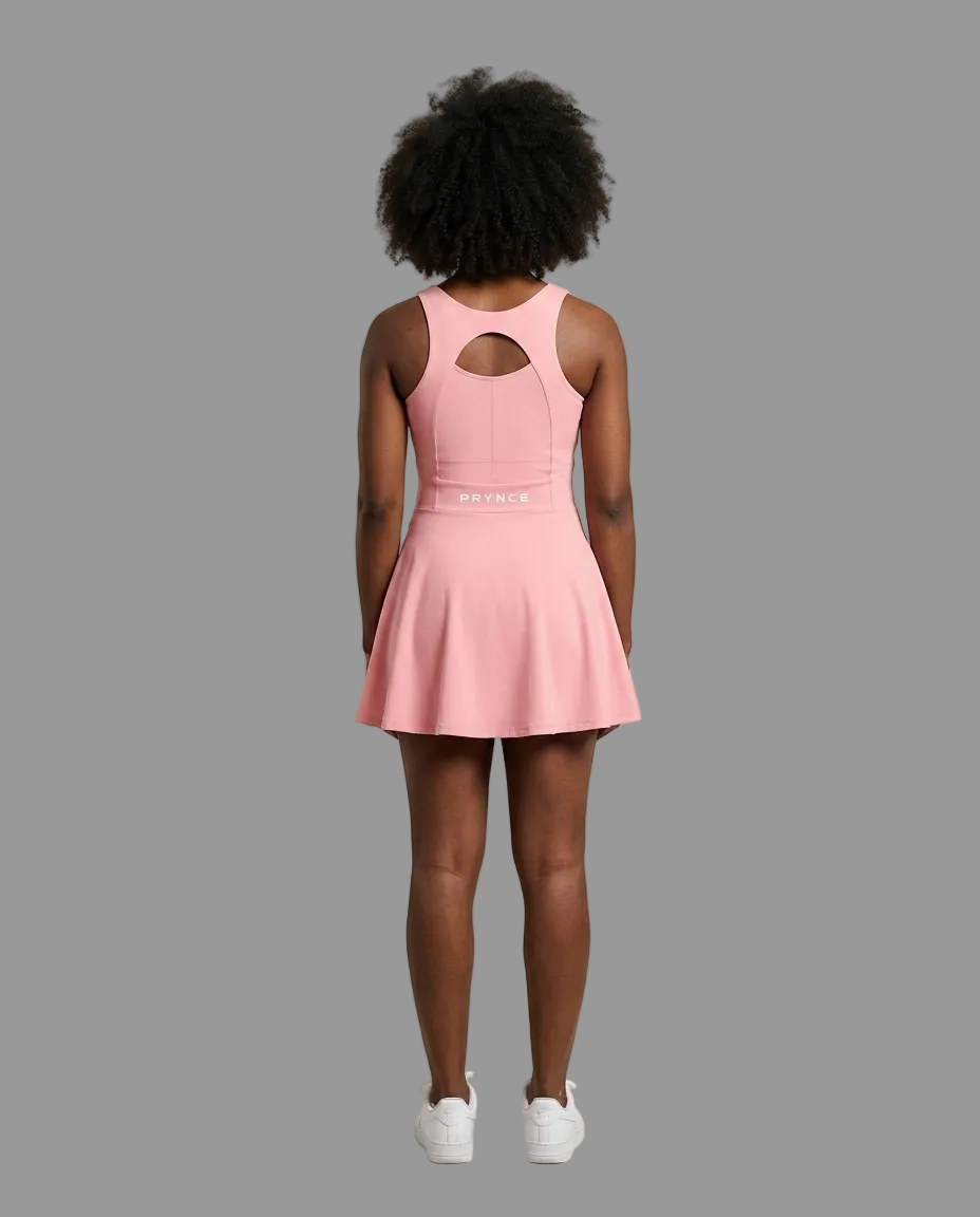 A model viewed from behind wearing a pink sleeveless athletic dress with a keyhole cutout at the back and a flared skirt, paired with white sneakers, against a solid light grey background.