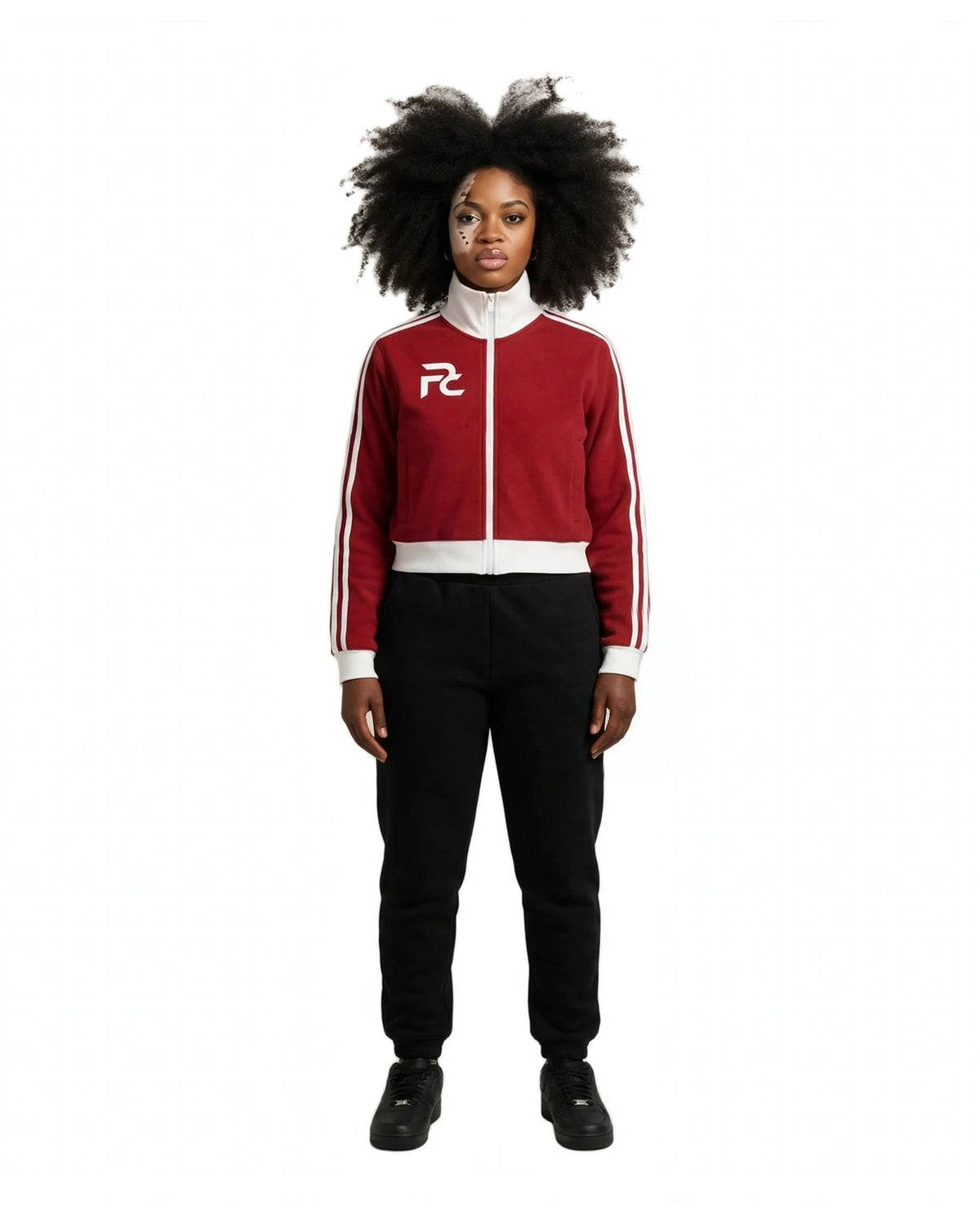 A model stands against a neutral beige studio background wearing a red and white track jacket with black sweatpants and black sneakers. The jacket features a white collar, white zipper, white side stripes, and a white 'RZ' logo on the left chest.