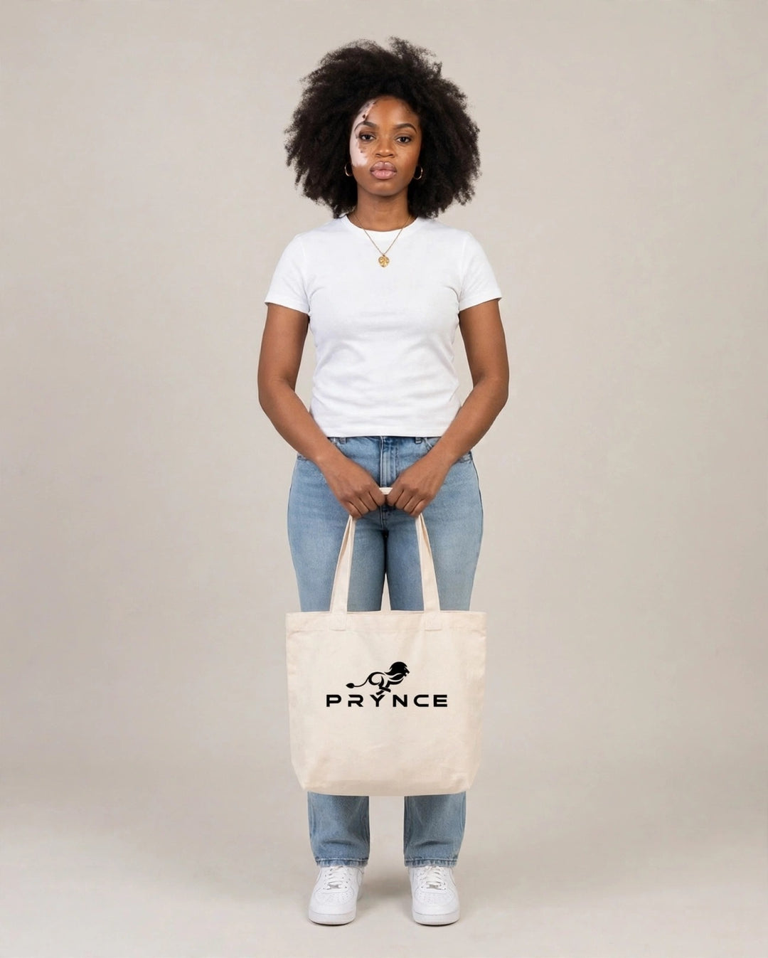 Camila holding the PRYNCE Lion Lockup Tote Bag in Cream with the black running lion logo, full body studio shot