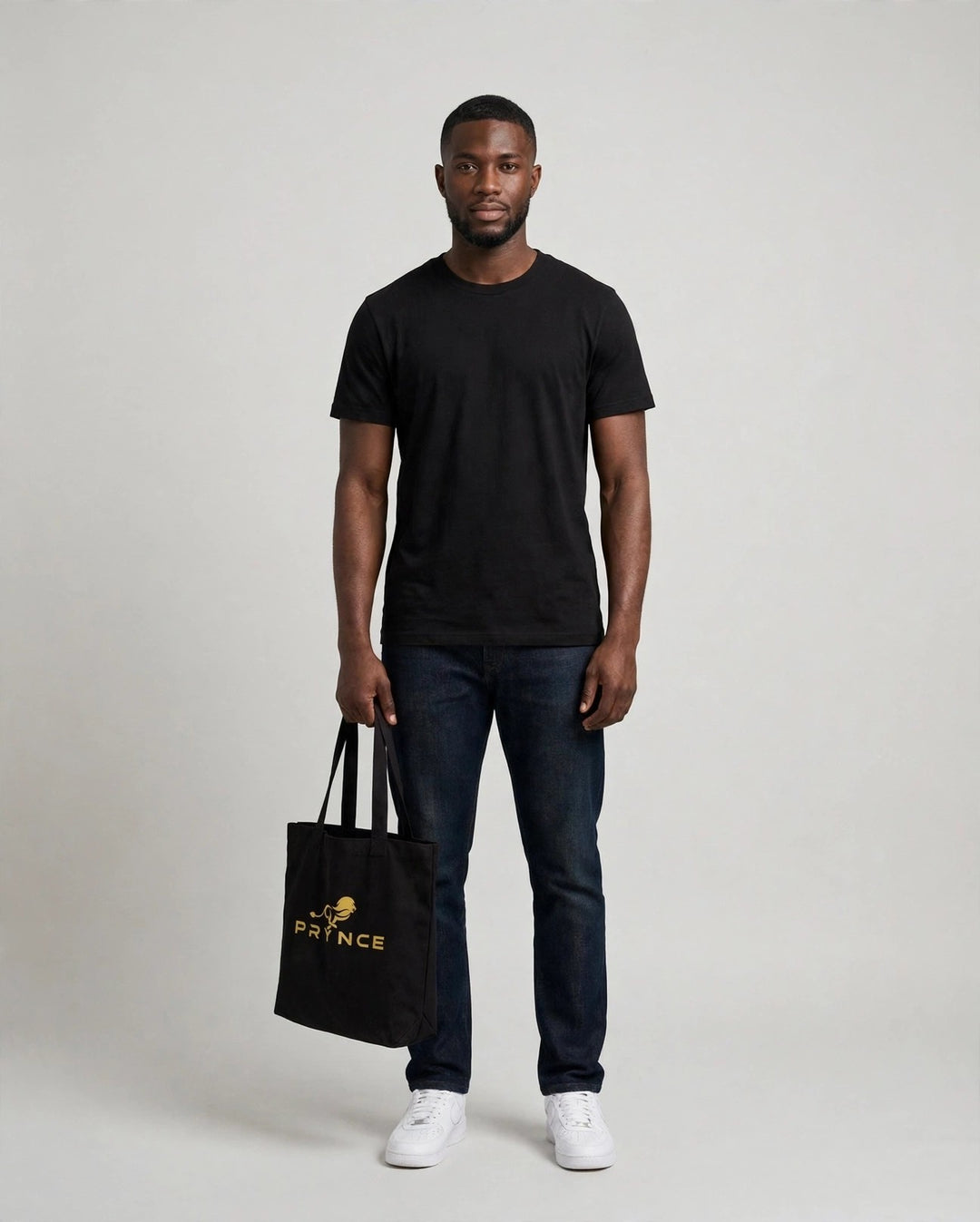 Chris holding the PRYNCE Lion Lockup Tote Bag in Black with the gold running lion logo, full body studio shot
