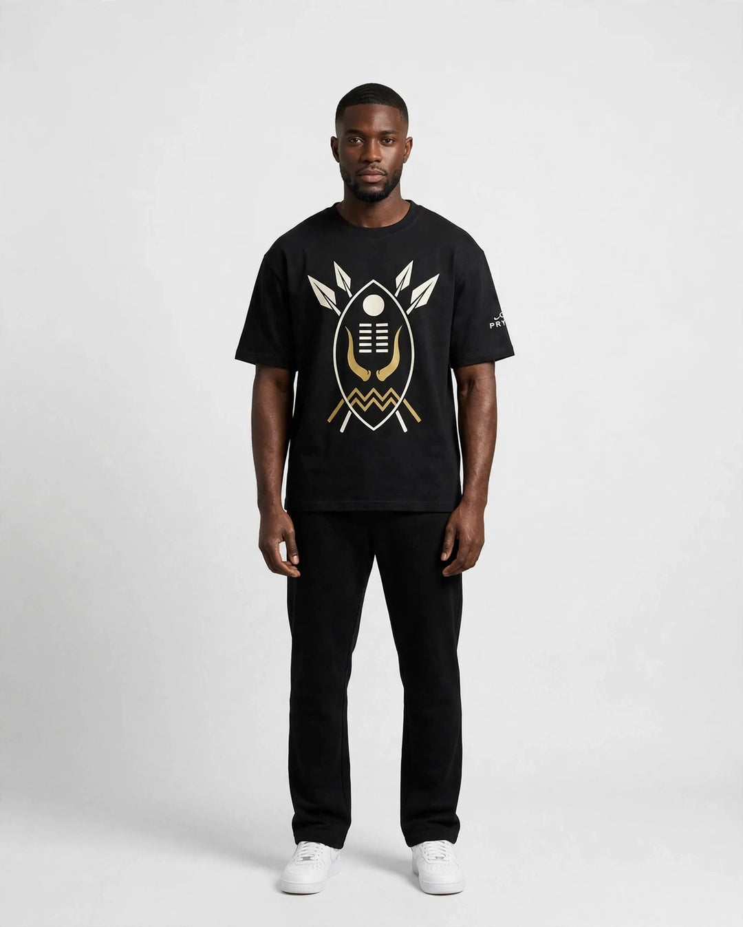 Chris wearing the PRYNCE AFRICA Warrior Shield Tee in black with cream and gold shield print, full body